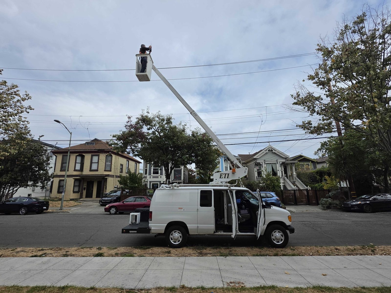 A white bucket van with the boom extended, raising a worker high above the street
